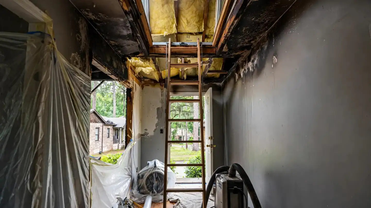 Open attic hatch with a ladder in a smoke-stained hallway